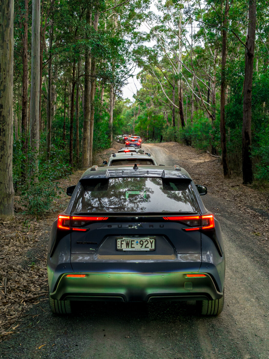 Grey 2026 Subaru Trailseeker electric SUV on a forest dirt track, rear view in a convoy