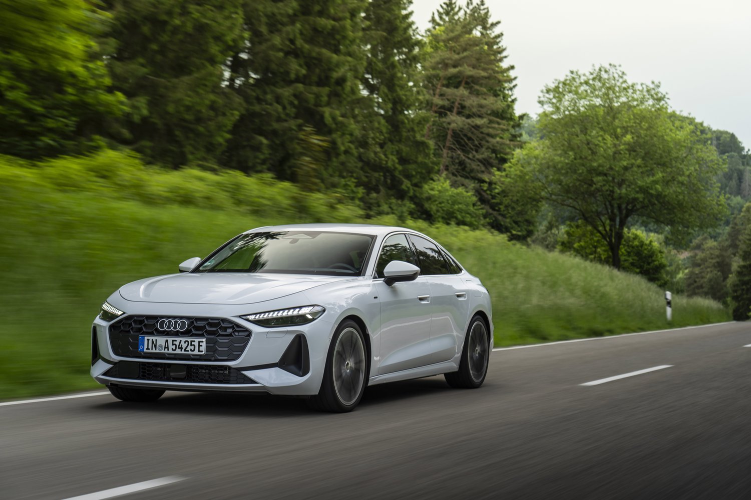 2026 Audi A5 e-hybrid quattro driving on a tree-lined country road, front three-quarter