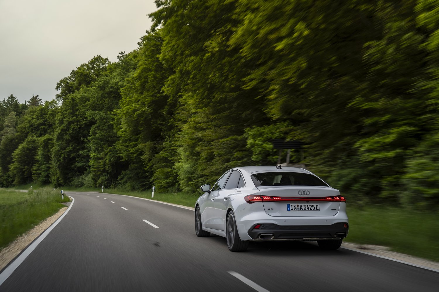2026 Audi A5 e-hybrid quattro driving on a forest road, rear three-quarter