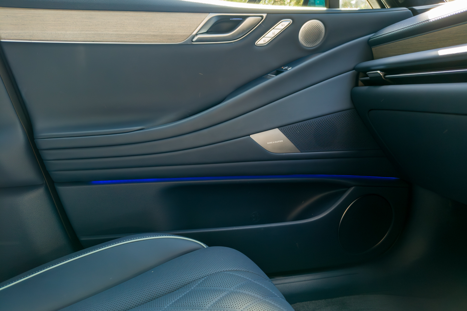 2026 Genesis G80 Electrified interior front door panel with blue ambient light strip and Bang and Olufsen speaker