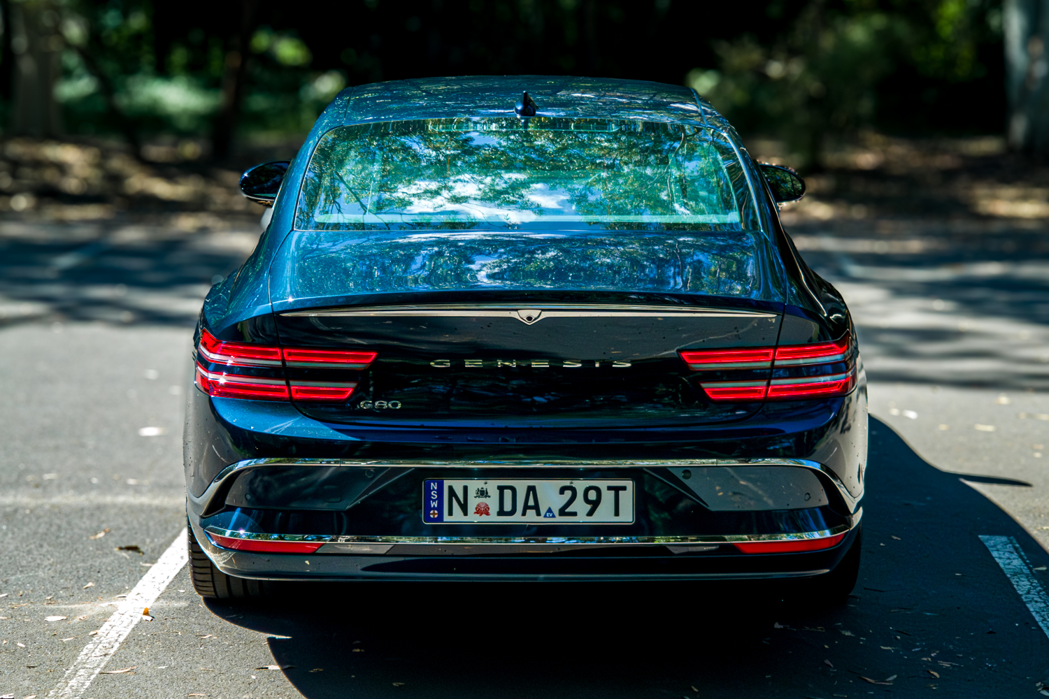 2026 Genesis G80 Electrified Matira Blue rear view in sunlight showing illuminated tail lights