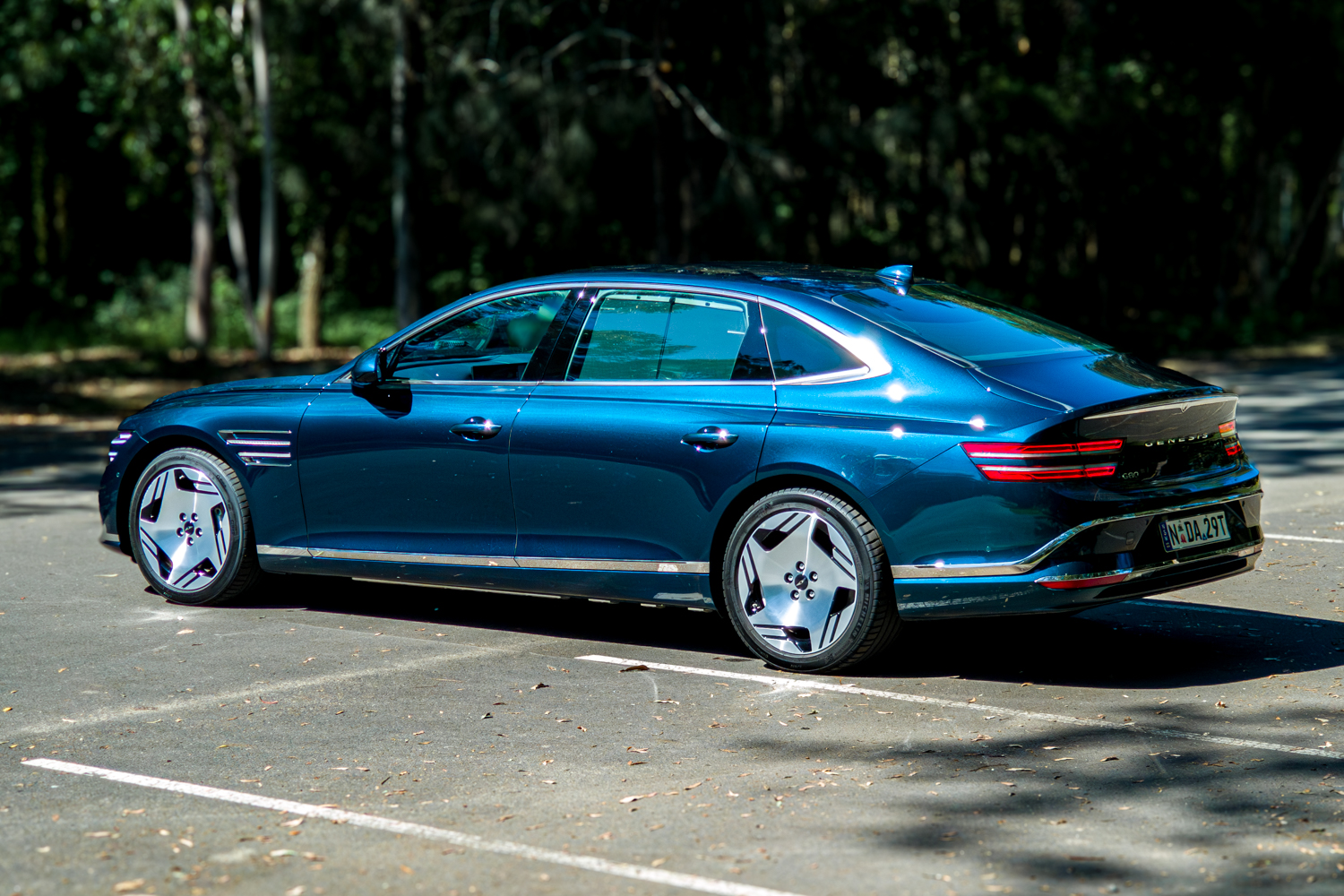 2026 Genesis G80 Electrified Matira Blue rear three quarter view from passenger side left in sunlight