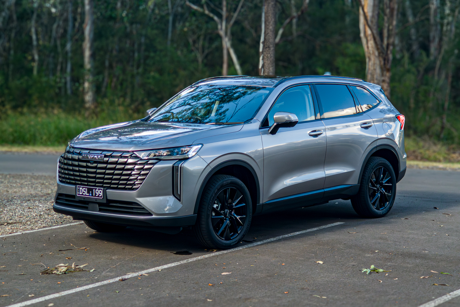 Front three quarter view of the grey 2026 GWM Haval H6 PHEV in a forest car park