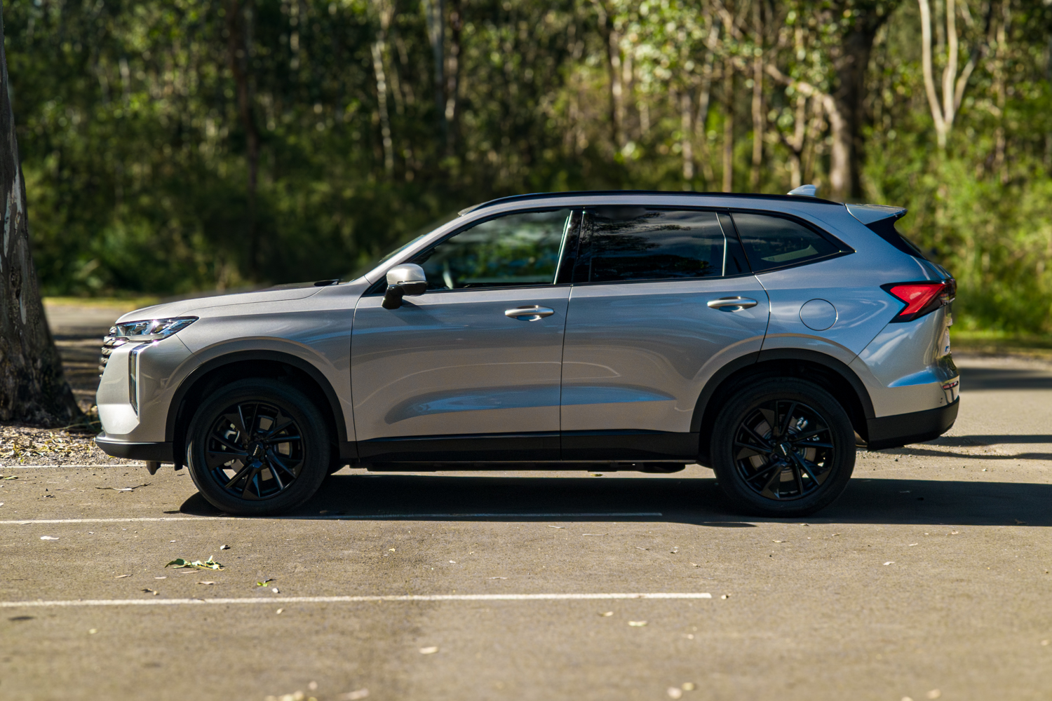 Passenger side profile of the grey 2026 GWM Haval H6 PHEV parked by trees