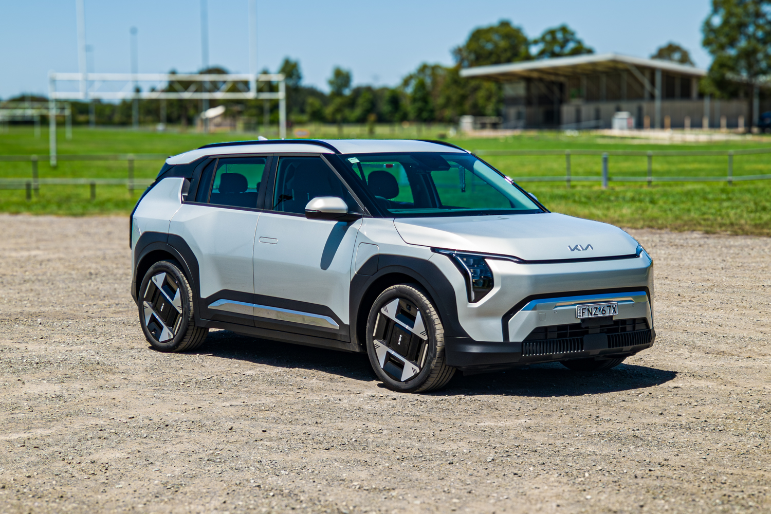 Front three-quarter angle of the silver 2026 Kia EV3 Earth Long Range on gravel with parkland behind