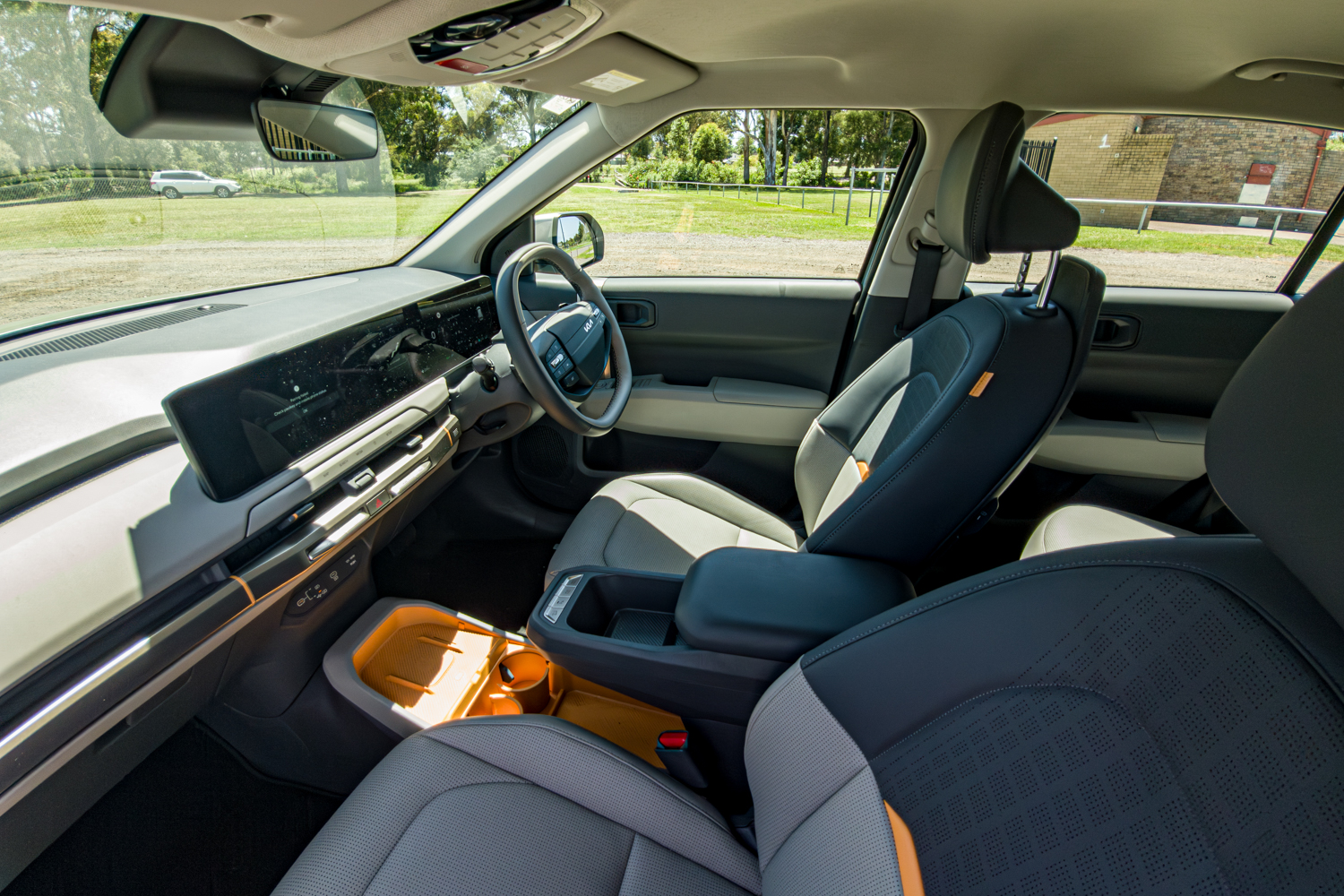 Front cabin of the 2026 Kia EV3 Earth Long Range showing dashboard, steering wheel and orange centre console tray