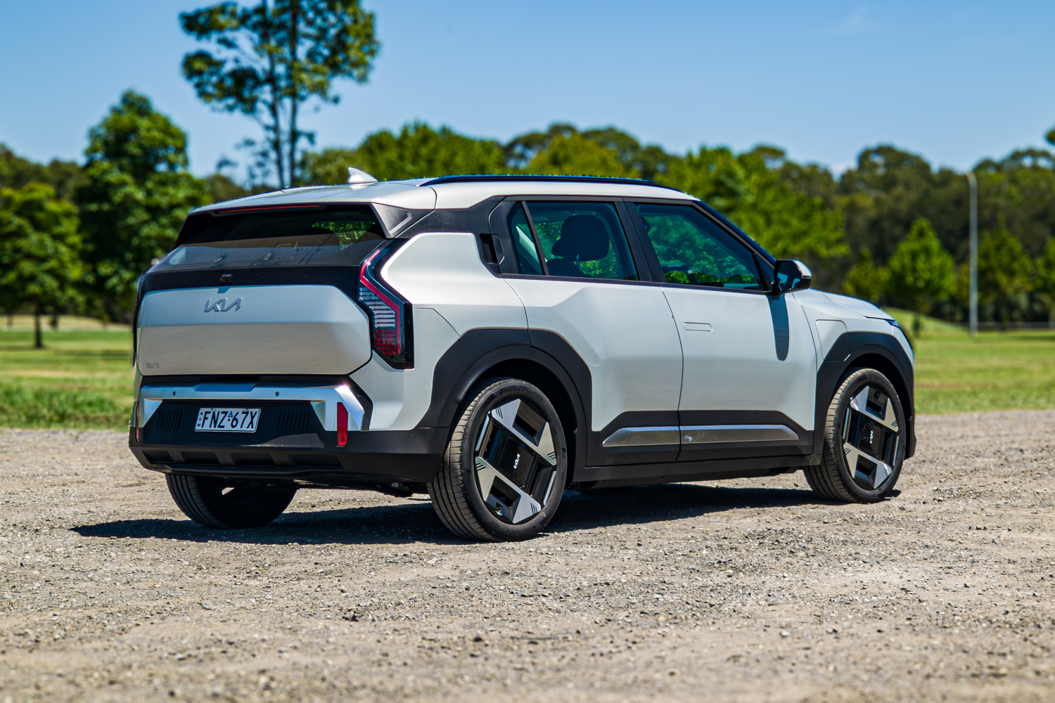 Driver's-side rear three-quarter view of the silver 2026 Kia EV3 Earth Long Range on grass