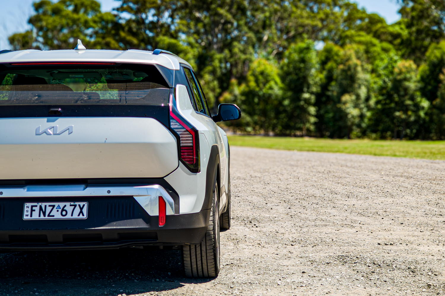 Rear three-quarter view of the silver 2026 Kia EV3 Earth Long Range from the driver's side on gravel