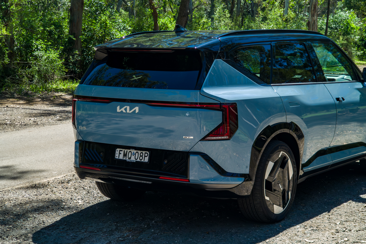 Rear three-quarter of the blue Kia EV5 GT-Line with the full-width LED tail lights illuminated
