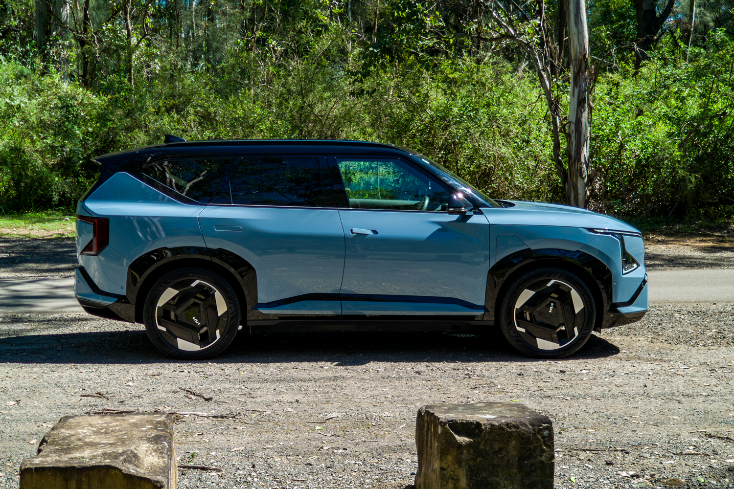 Full driver-side profile of the blue Kia EV5 GT-Line electric SUV on a gravel road