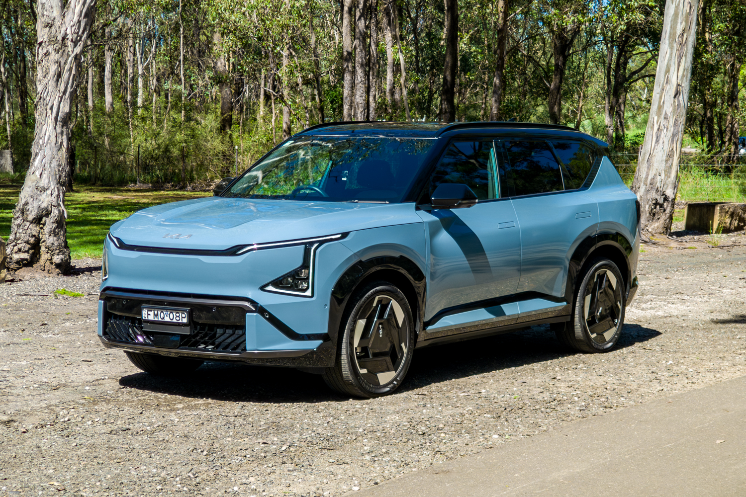 Front three-quarter of the blue Kia EV5 GT-Line from the passenger side among gum trees