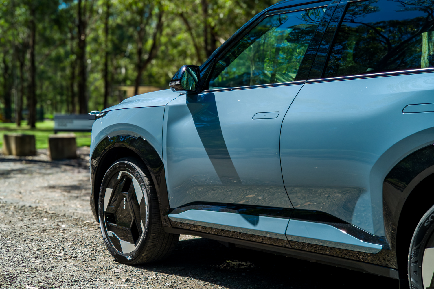Side detail of the blue Kia EV5 GT-Line showing the gloss-black side skirt and front wheel