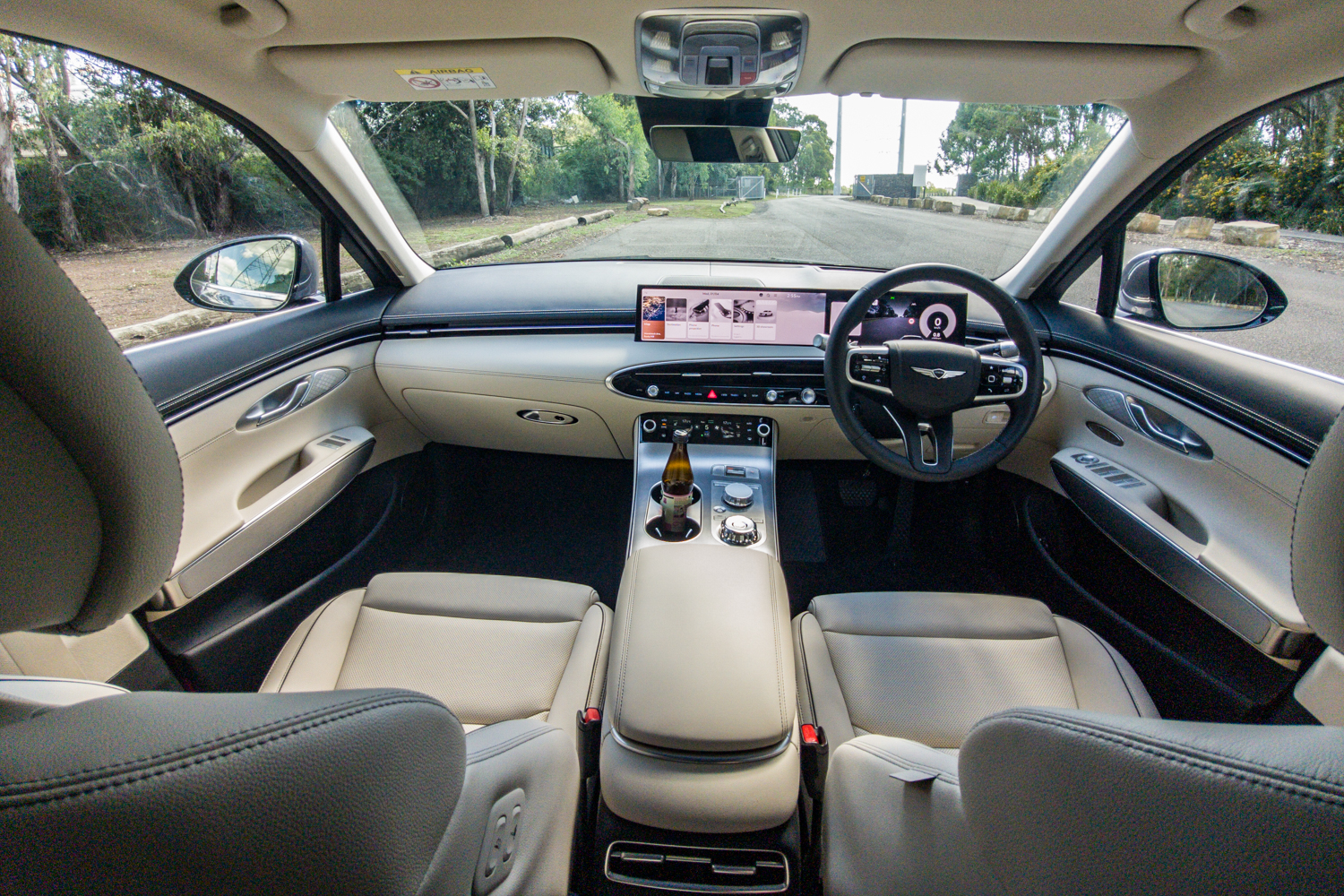 Wide-angle view of the 2026 Genesis GV70 2.5T Advanced cabin from the rear seat showing the cream leather and 27-inch display