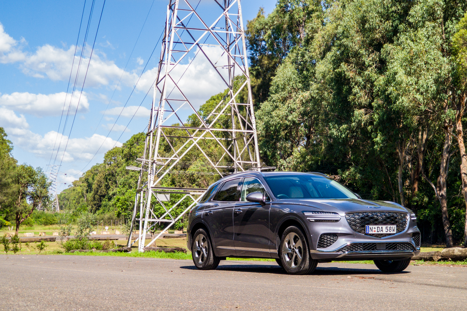 Wide front three-quarter of the 2026 Genesis GV70 2.5T Advanced beside a power pylon and gum trees