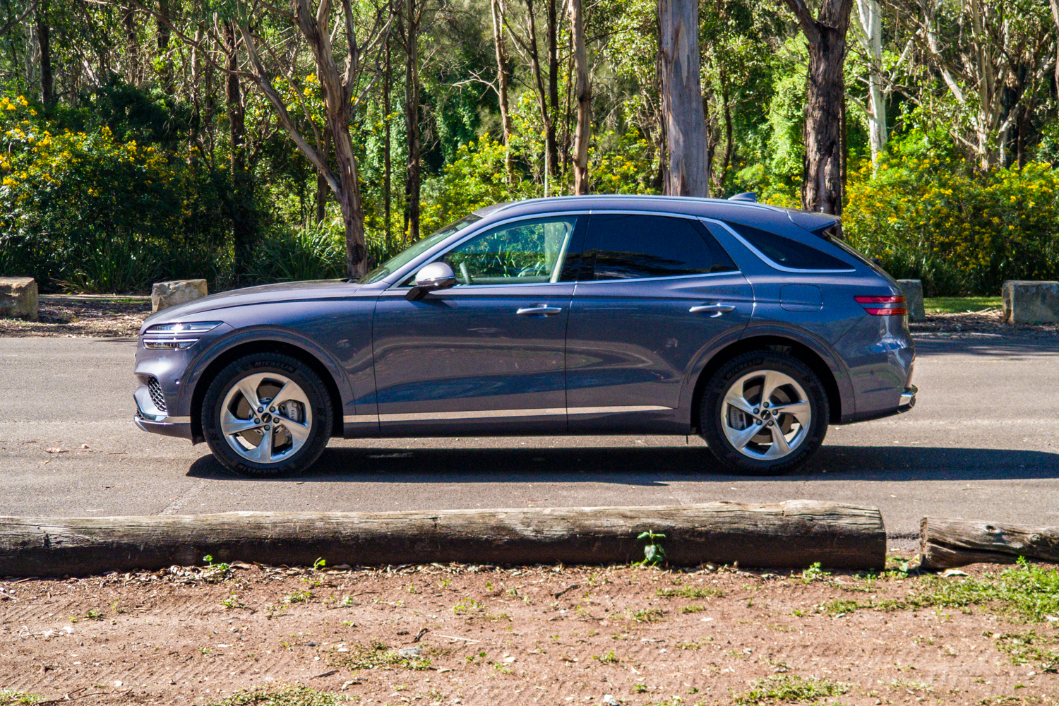 Passenger's-side profile of the 2026 Genesis GV70 2.5T Advanced with wattle in bloom behind