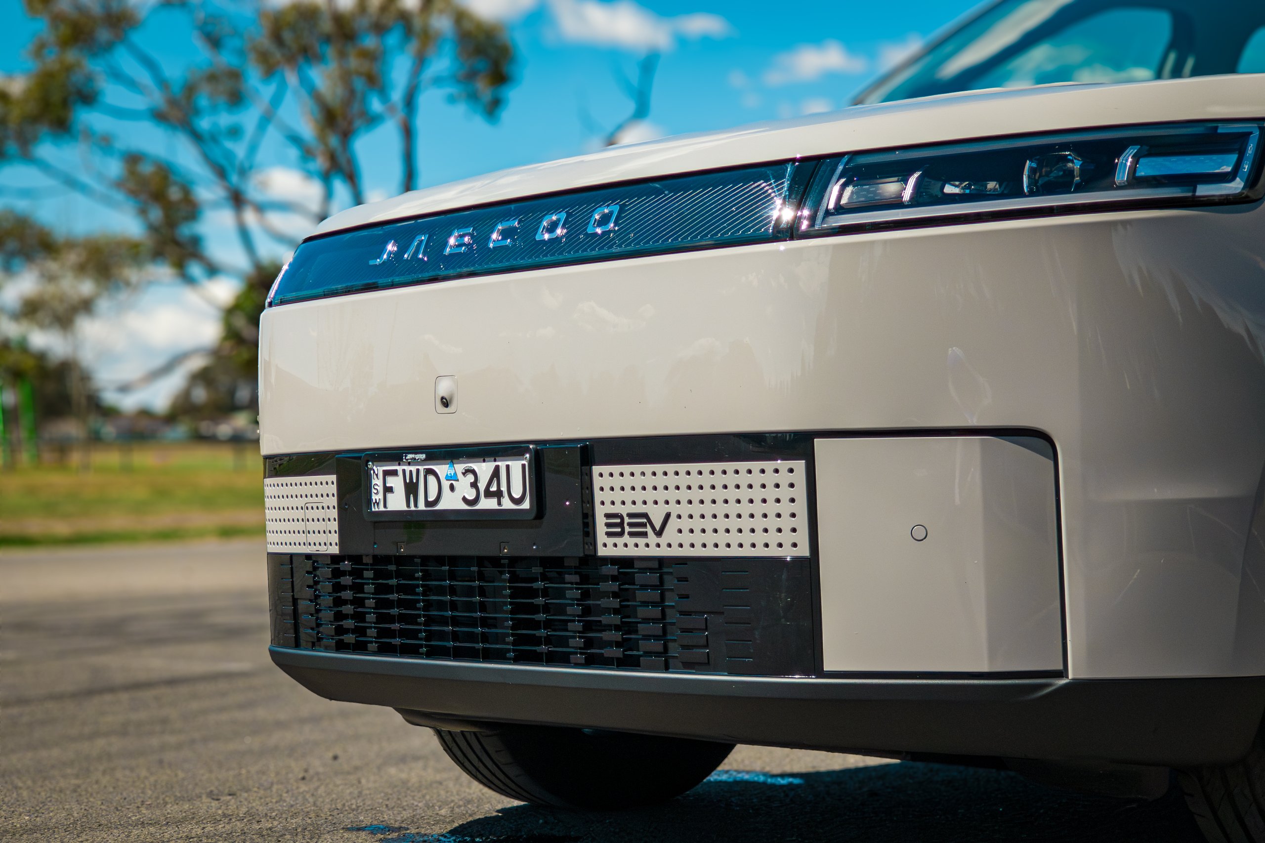 Low close-up of the front of the Stone Grey 2026 Jaecoo J5 EV Summit showing JAECOO lettering, headlights and BEV grille plate