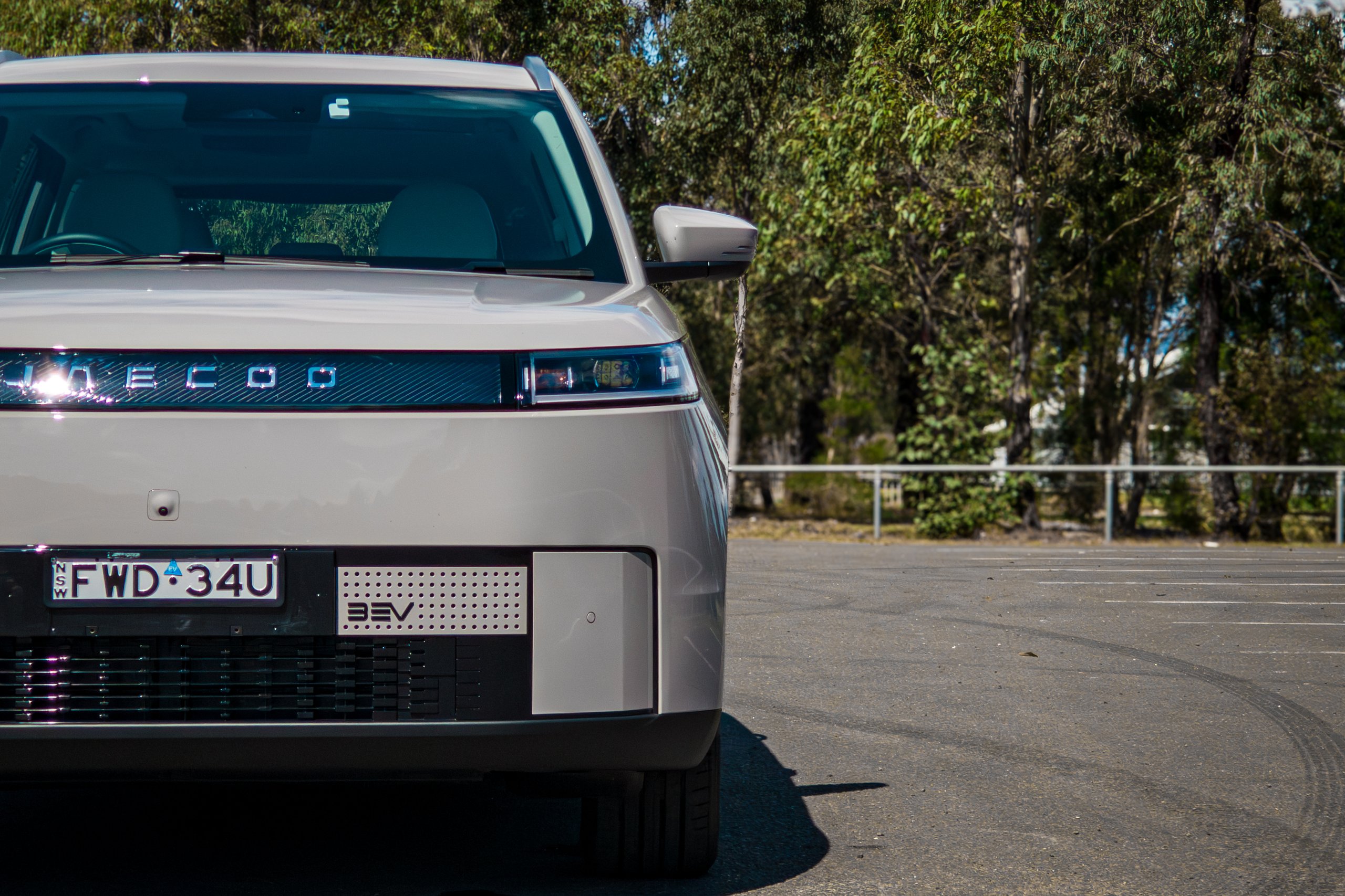 Passenger-side headlight and front corner of the Stone Grey 2026 Jaecoo J5 EV Summit with a car park behind