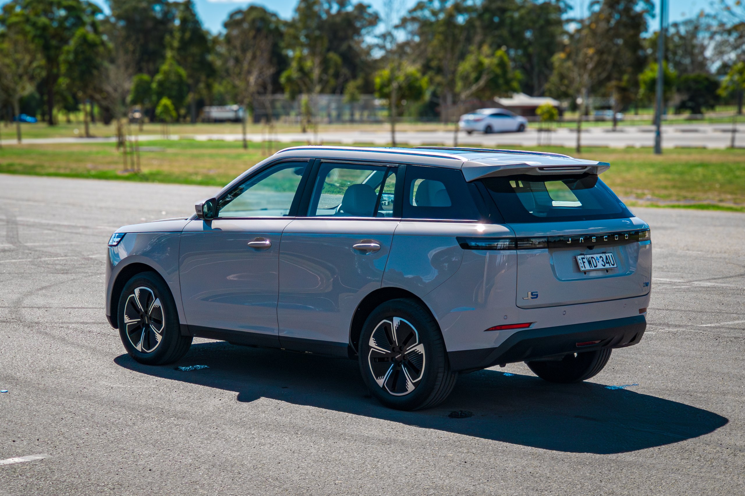 Driver-side rear three-quarter of the Stone Grey 2026 Jaecoo J5 EV Summit from a high angle with a sports field behind