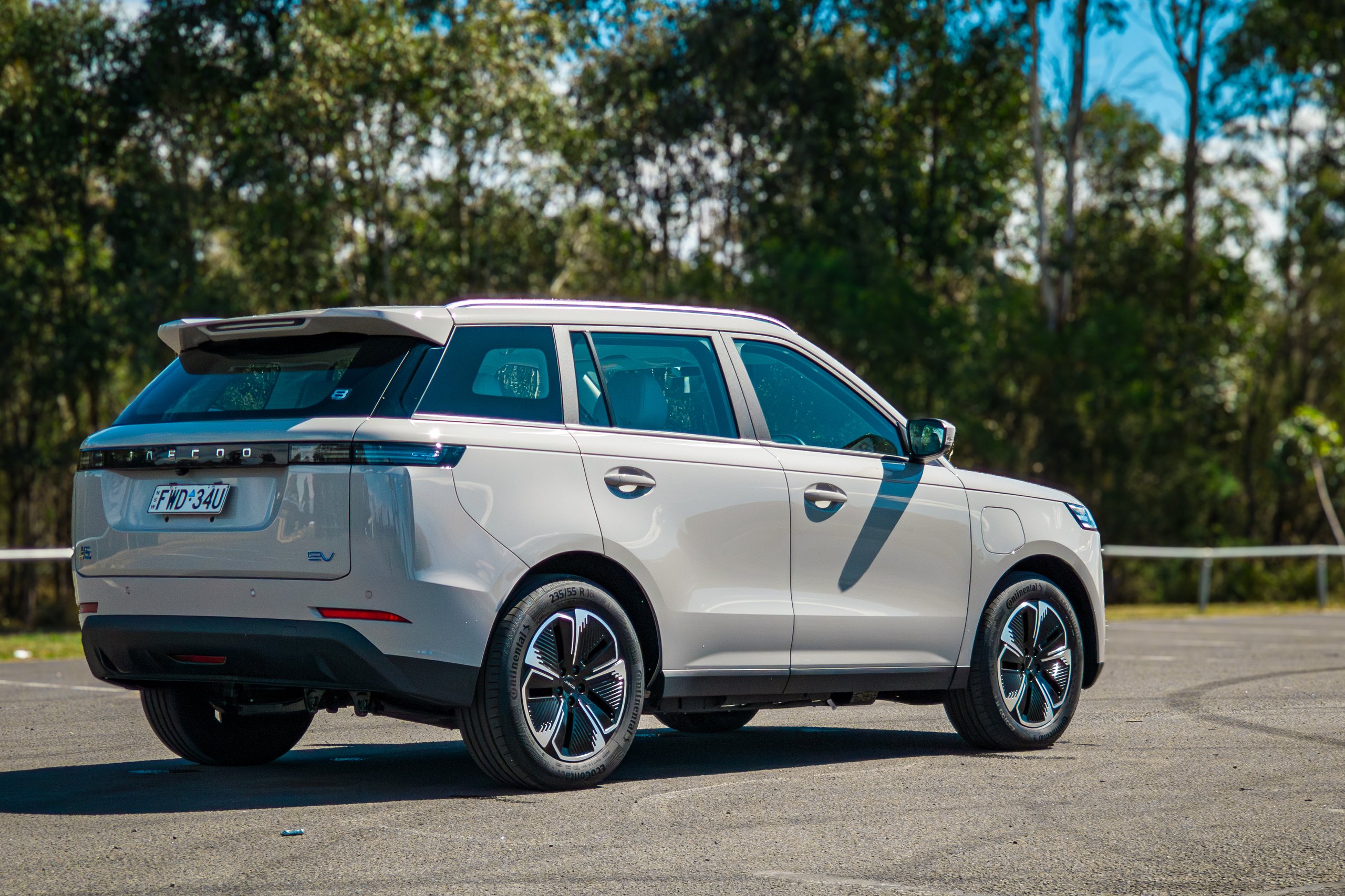 Passenger-side rear three-quarter of the Stone Grey 2026 Jaecoo J5 EV Summit against a treeline and blue sky