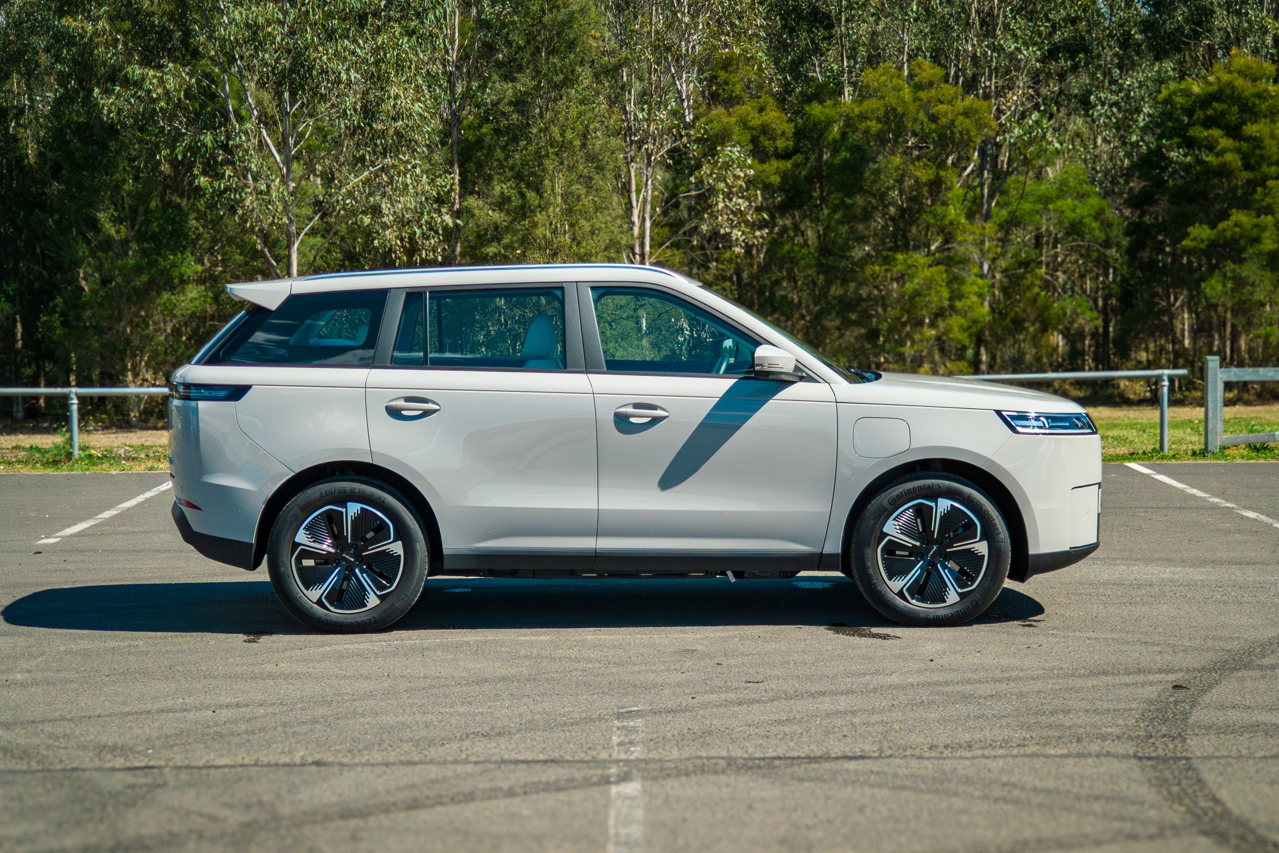 Full driver-side profile of the Stone Grey 2026 Jaecoo J5 EV Summit parked in front of gum trees