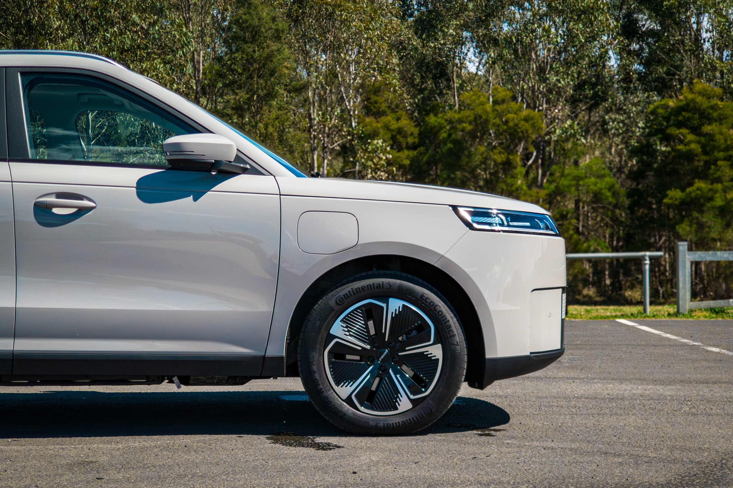 Driver-side profile of the front half of the Stone Grey 2026 Jaecoo J5 EV Summit showing the front wheel, mirror and charge flap