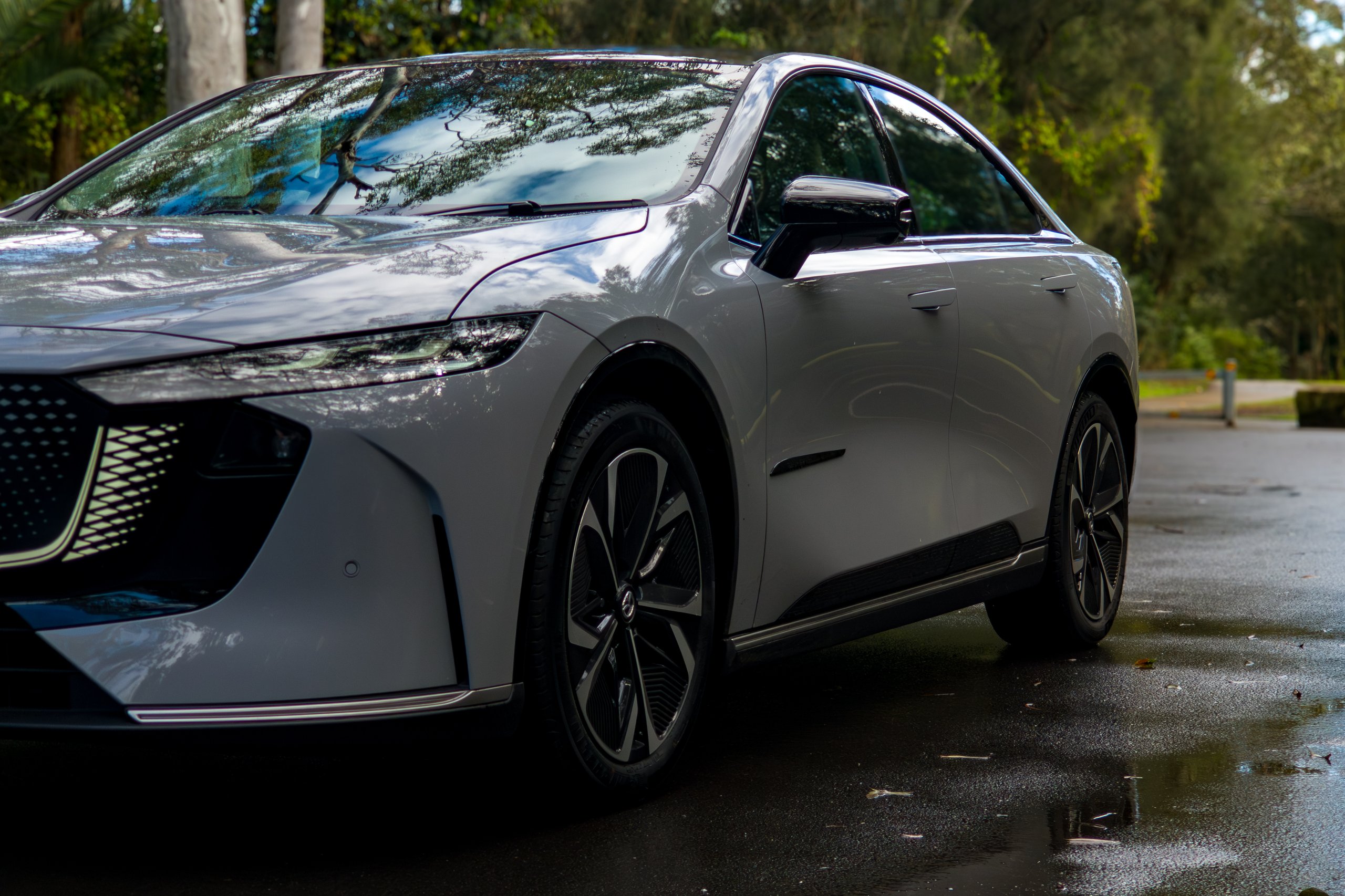 Low front three-quarter angle of the light grey 2026 Mazda 6e GT on wet bitumen