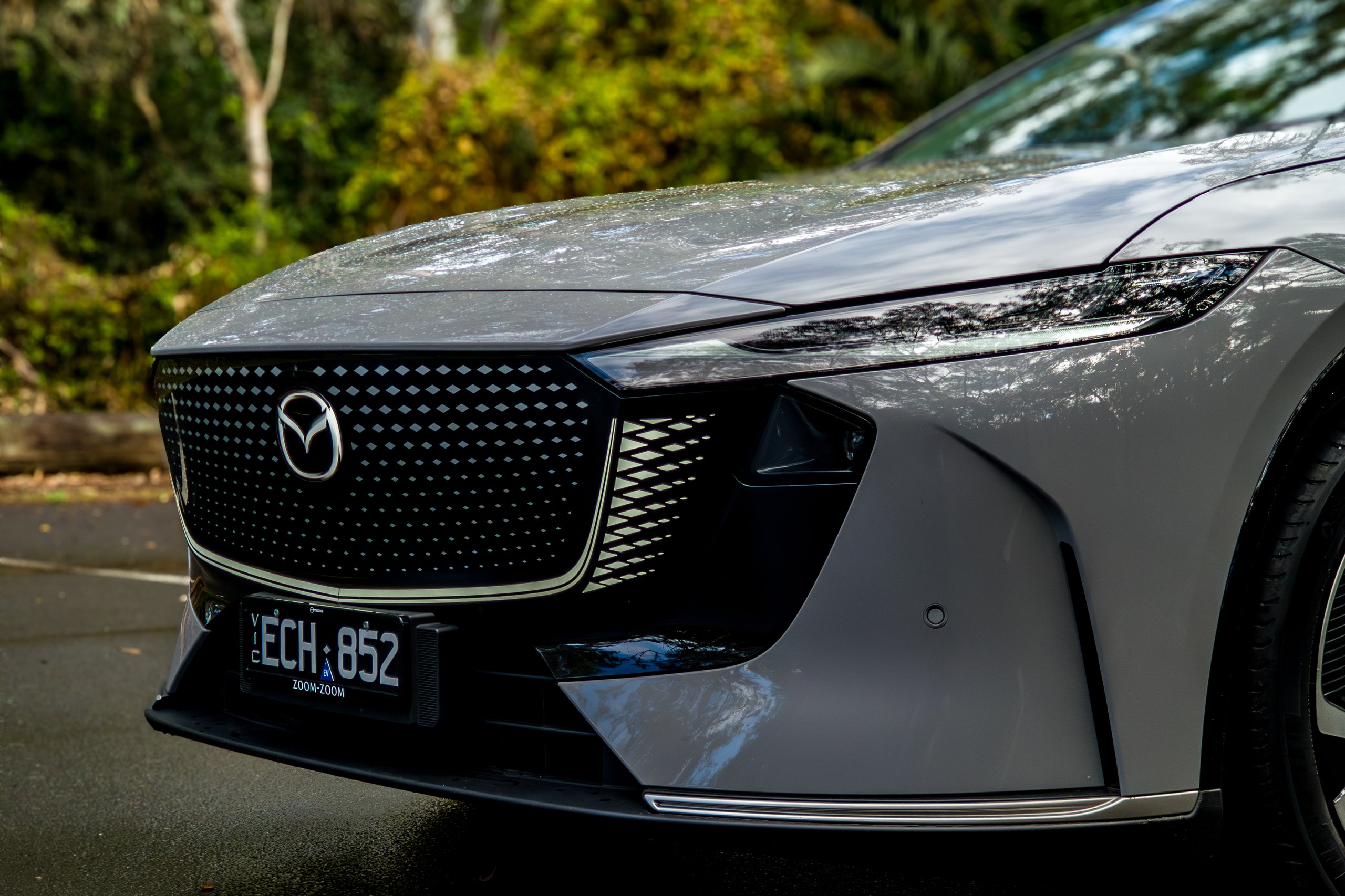 Angled close-up of the 2026 Mazda 6e GT closed grille panel, Mazda badge and headlight