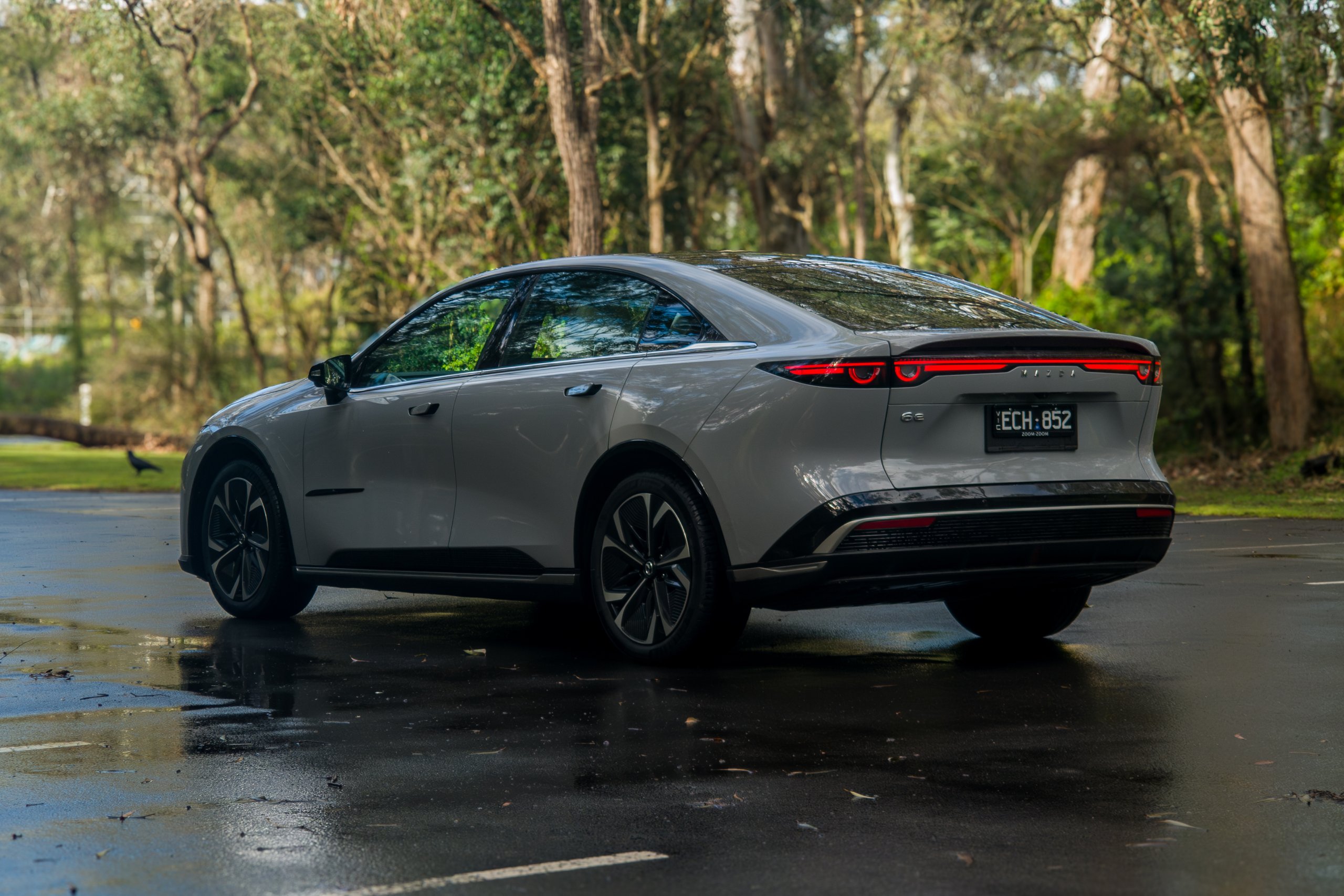 Rear three-quarter passenger-side view of the light grey 2026 Mazda 6e GT on a wet road