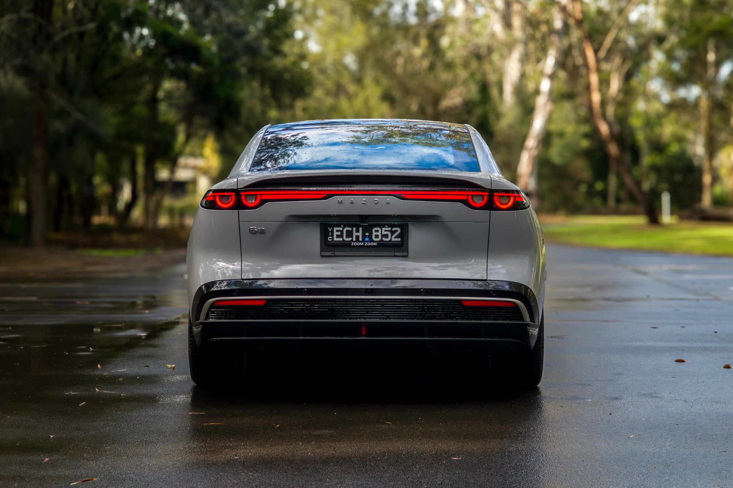 Straight-on rear view of the light grey 2026 Mazda 6e GT with tail lights illuminated